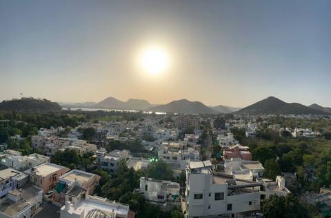      Panoramic view of a city with mountains and the sun setting in the background.
  