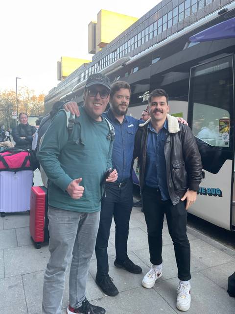 Three people posing in front of a tour bus.