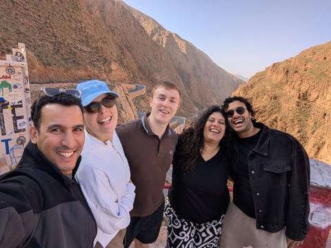 Group smiling with a scenic winding road and cliffs in the background.