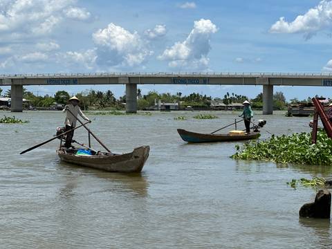       Two people rowing boats on a wide river.
  