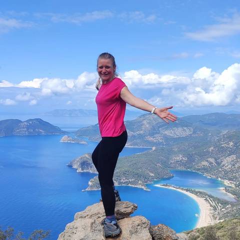 Person posing with arms outstretched against a coastline view.