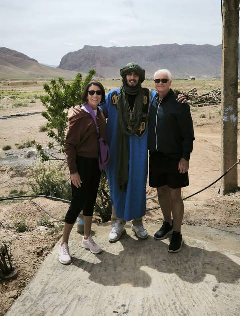 Three people posing with a local in traditional attire.