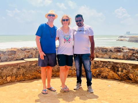 Three people posing in front of a stone wall by the sea.