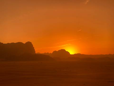 Sunset over desert landscape with silhouetted rocks.