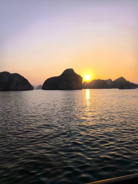 Sunset over Halong Bay with traditional boat on the water.