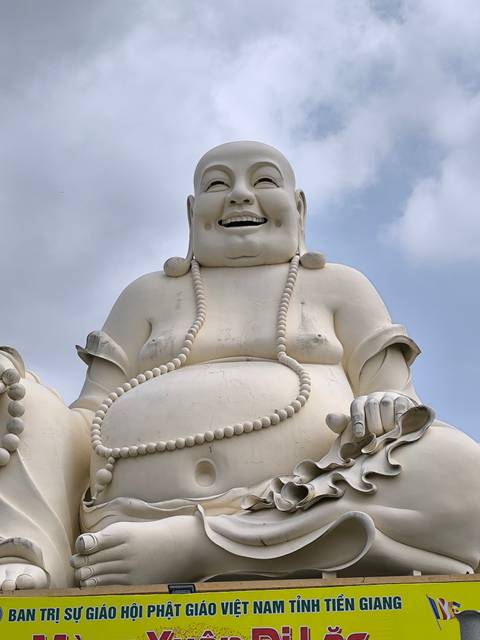 Large white Buddha statue with a smile and prayer beads.