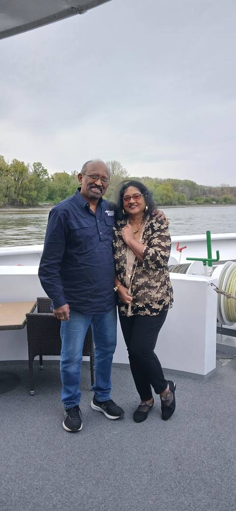 Two people smiling on a boat with a river in the background.