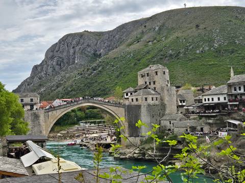       People walking on historic bridge with mountains in the background.
  