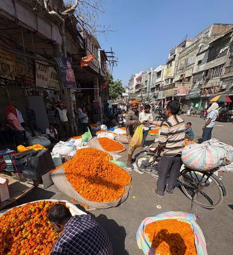 Busy market street with vendors and colorful flowers.