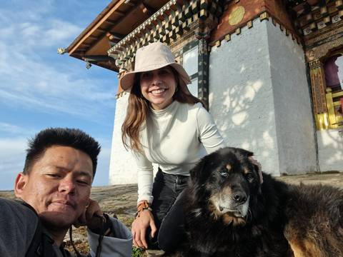       Couple with a dog in front of a traditional Bhutanese building.
  