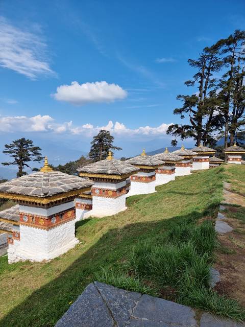       Chortens at Dochula Pass under a blue sky with mountains in the distance.
  