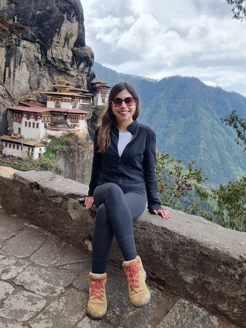      Woman sitting on a ledge with Taktshang Monastery in the background.
  