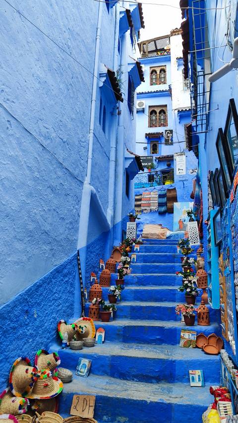       Vibrant blue street with colorful textiles in Chefchaouen.
  