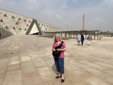 A person standing in front of a modern museum with an obelisk.