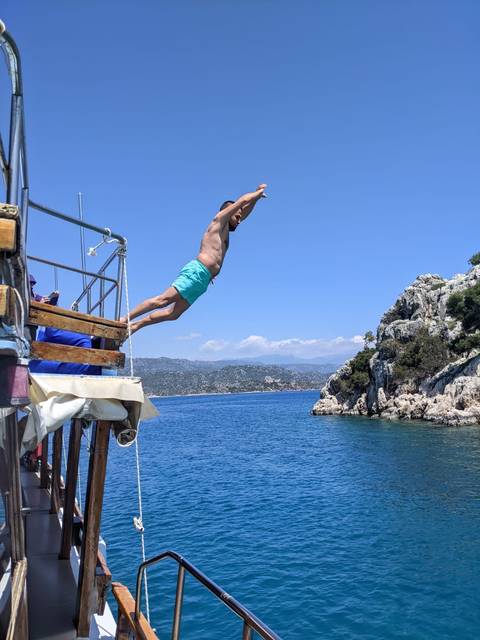 Man diving into the sea from a boat with cliffs in the background.
