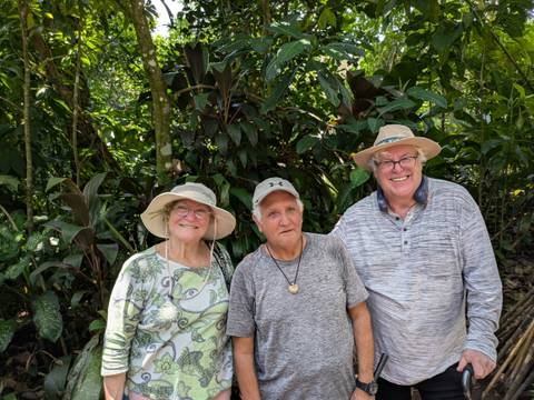 Three elderly people smiling in a lush forest setting.