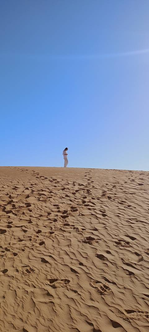 Person walking on sand dunes with footprints.