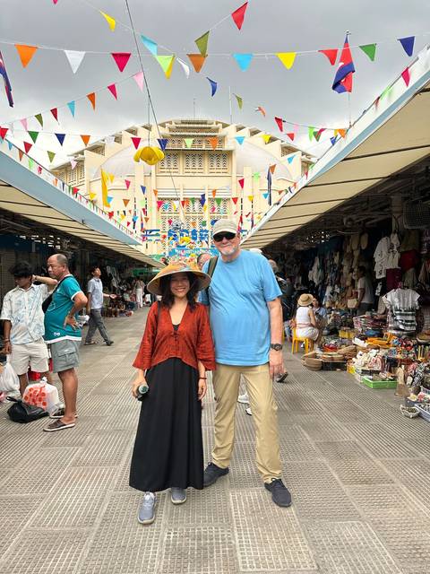 Two people posing in a vibrant market with colorful decorations.