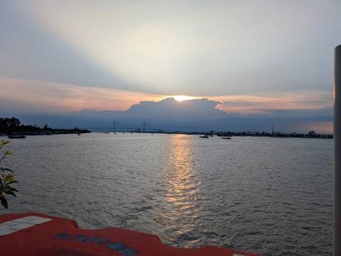 Sunset over a river with boats and a bridge in the distance.