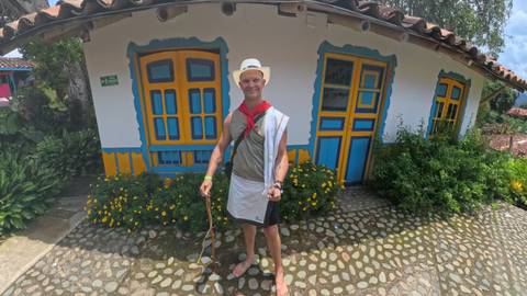       Man in traditional attire in front of a colorful house.
  