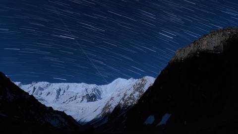 Star trails in a clear night sky over snowy mountains.