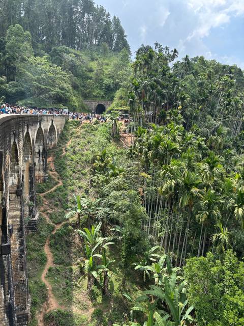       People on the Nine Arches Bridge over lush vegetation.
  