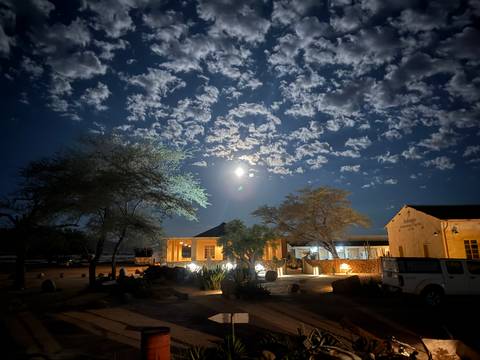       A well-lit lodge under a night sky with scattered clouds and a visible moon.
  