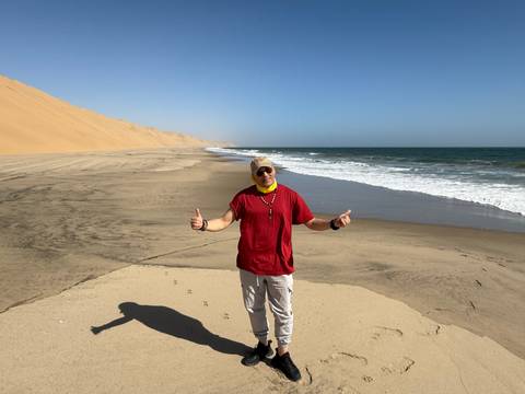       Person on a beach with waves and sandy dunes under a clear blue sky.
  