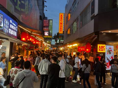       Crowded night market street with illuminated signs.
  