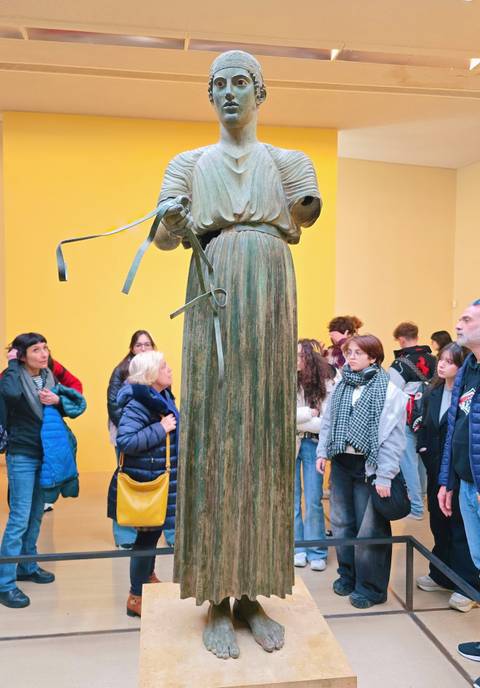 Visitors observing a large ancient bronze statue.