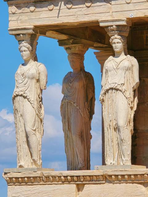 Three Caryatid statues against a blue sky.