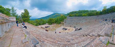 Ancient theater with people sitting on steps.