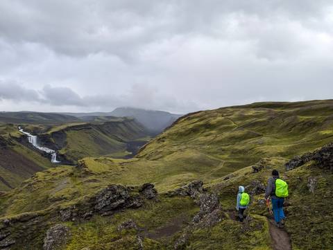 Hikers viewing a waterfall in a vast green landscape.