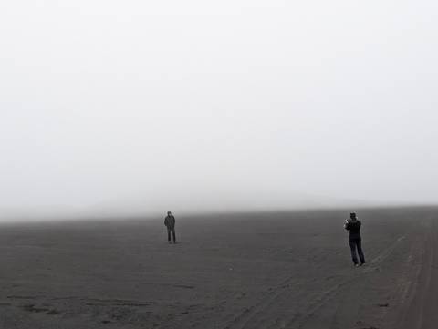 Foggy landscape with two people standing on dark terrain.