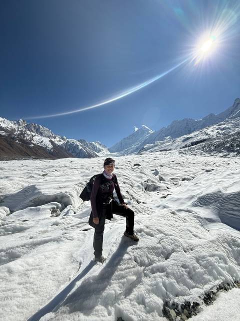Person sitting on a glacier beneath a clear blue sky.