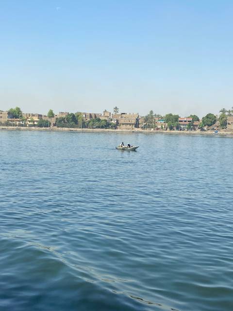 Two people in a small boat on a river with distant buildings.