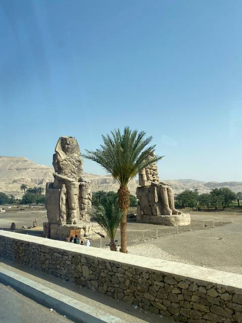 Two large stone statues with a palm tree in front.