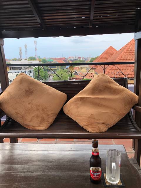 View from a terrace with two cushions on a bench overlooking city rooftops.