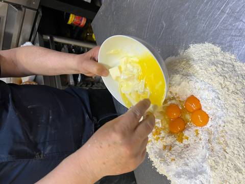 Someone preparing dough with egg yolks and flour in a kitchen.