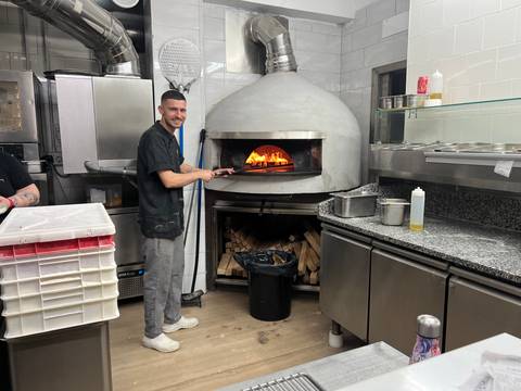 A man baking pizza using a traditional wood-fired oven.