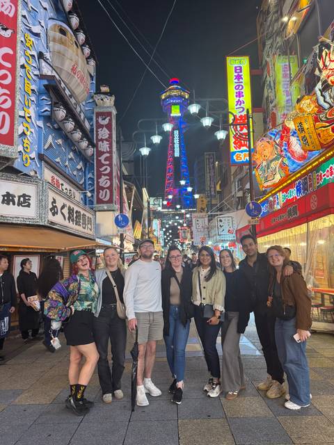       Group of people posing at night in a busy city street with neon lights.
  
