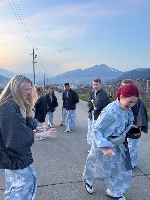       People wearing traditional attire outdoors with mountains in the background.
  