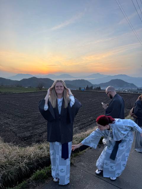       Person standing in a field with mountains at sunset.
  