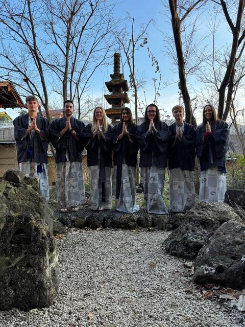       Group of people wearing traditional attire, standing in a garden area.
  