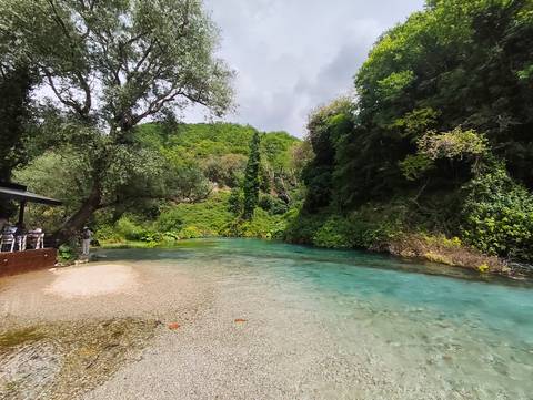       River surrounded by green vegetation with people on the left side.
  