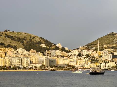 Coastal cityscape with boats and buildings against a mountainous backdrop.