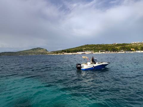 Man on a boat in a coastal area with hills in the background.