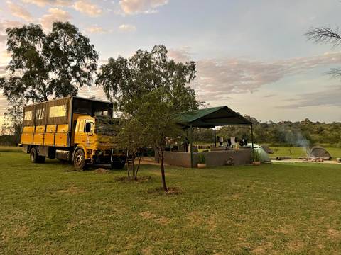 A camping area with a large yellow truck and smoke from a small fire at sunset.