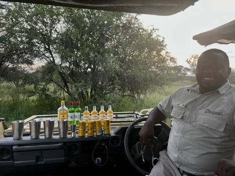 A man standing next to a safari vehicle with drinks displayed on the bonnet.