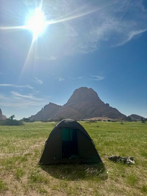 A tent with a backdrop of a towering rock formation under a clear blue sky.
